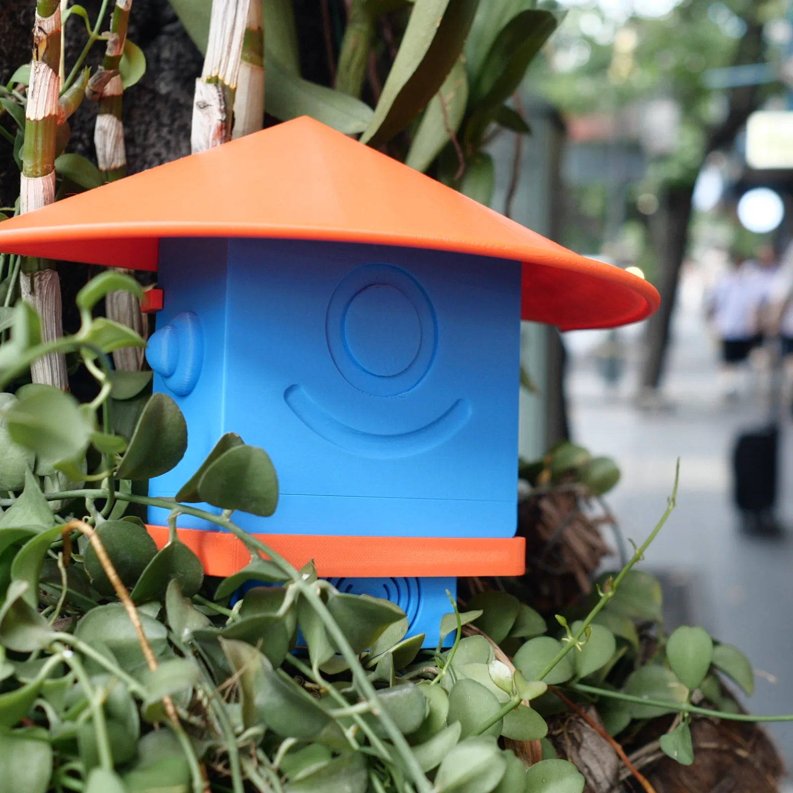 A blue Altruist half-hidden in creeping greenery, a Bangkok pavement behind it