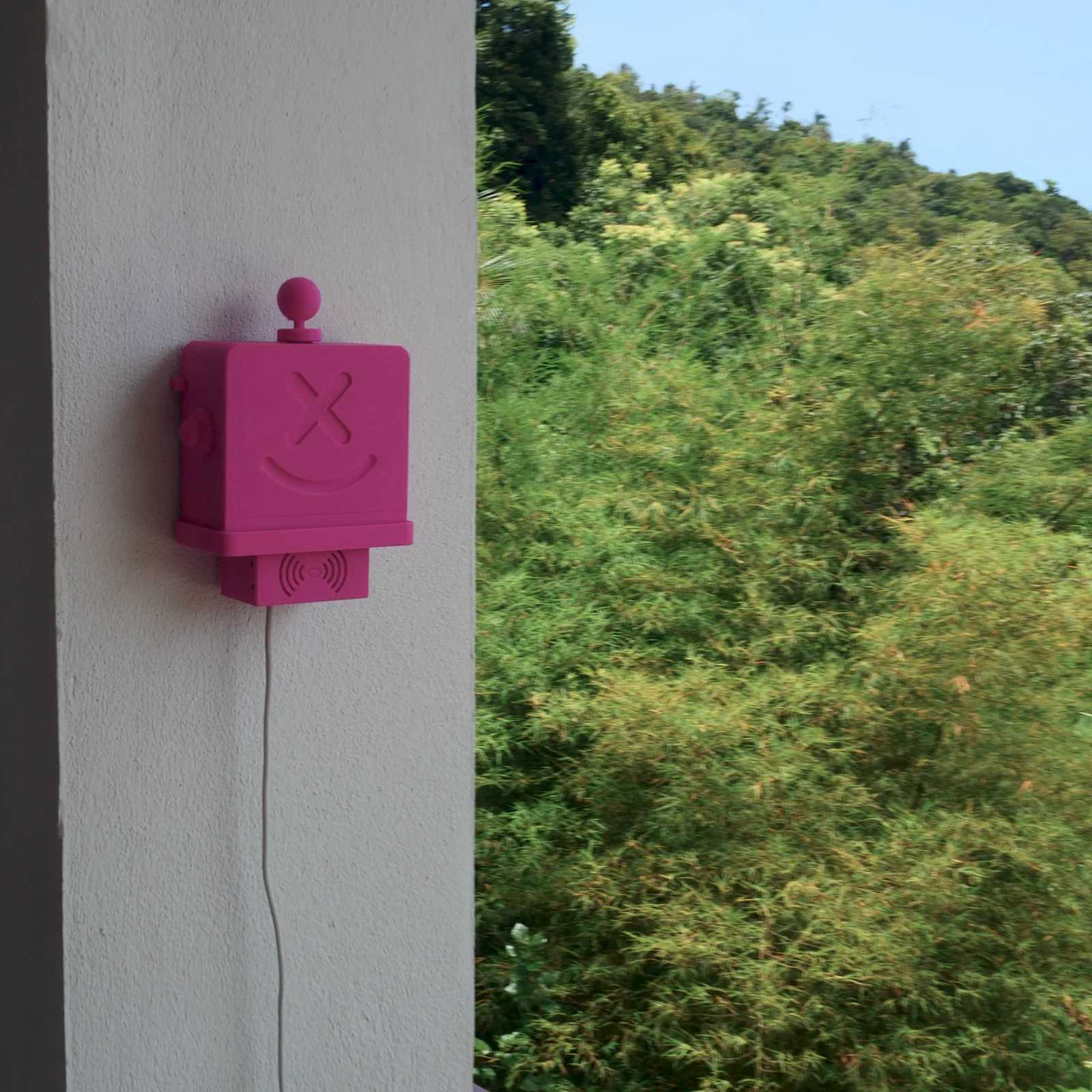 A pink Altruist on a white wall with the jungle-covered hills of Koh Phangan behind