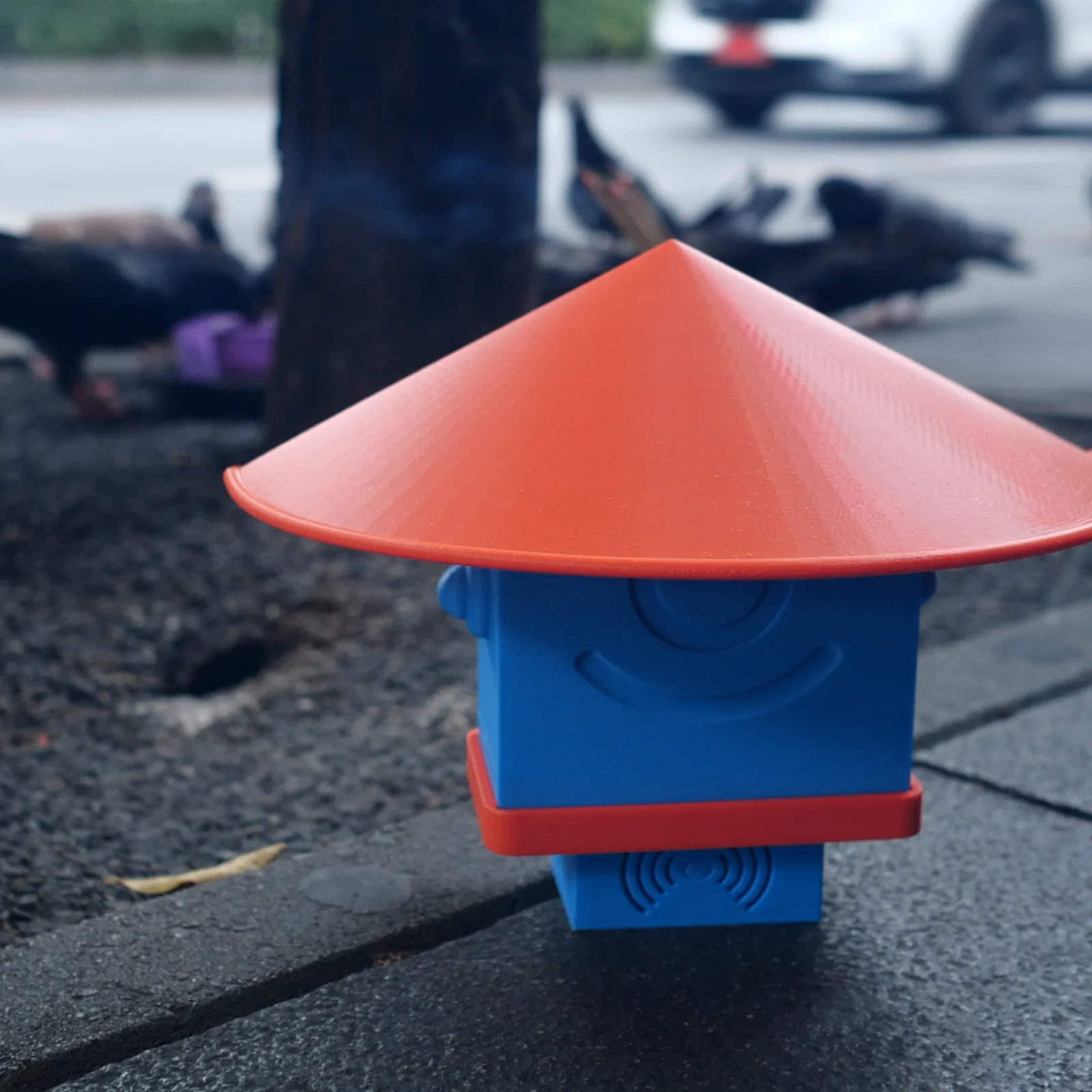 A blue Altruist standing on the pavement, pigeons resting under a tree behind it