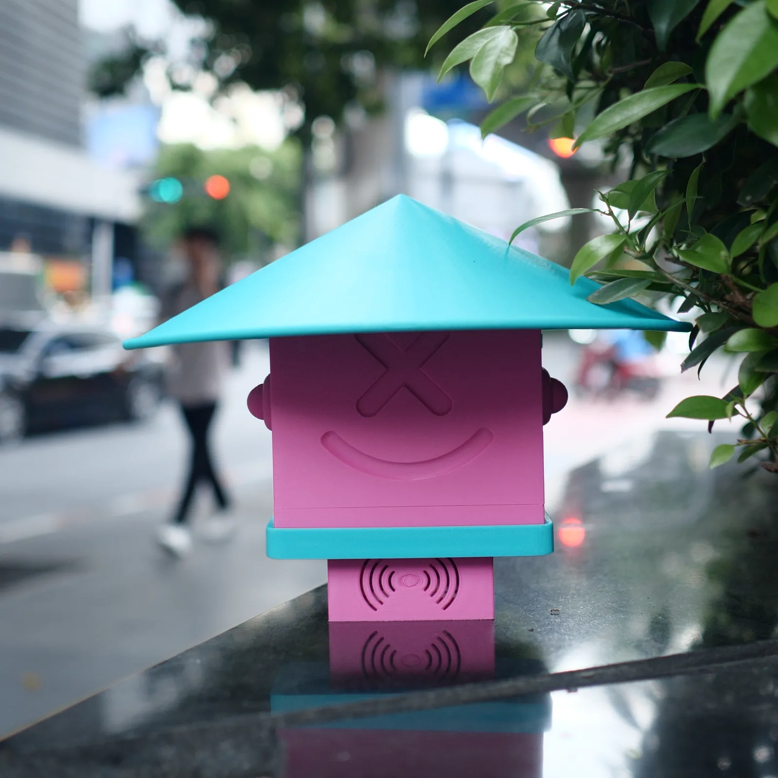 A pink Altruist with a turquoise roof on a wet glass table, rain-blurred street behind it