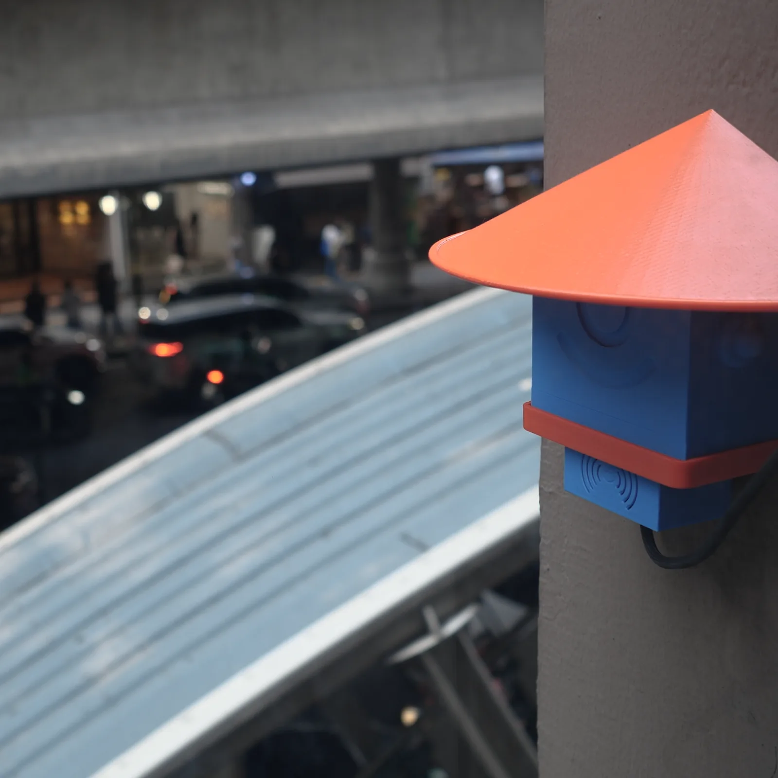 A blue Altruist on a wall at dusk, the curved roof of a skytrain station behind it