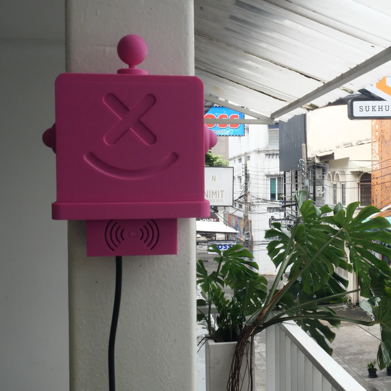 A pink Altruist on a column, monstera leaves and shopfronts behind it
