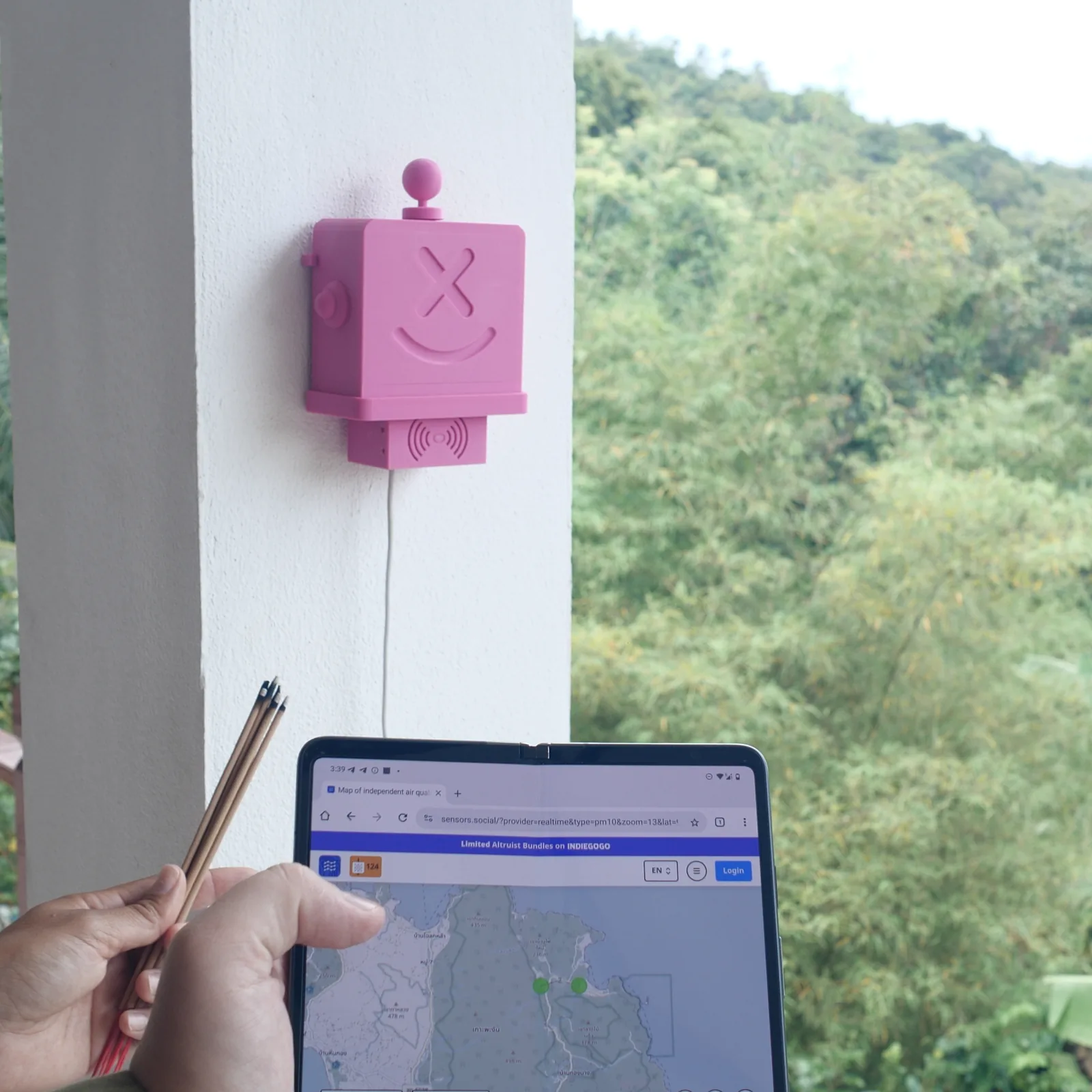 A hand holding a tablet with the sensors.social map of the island, a pink Altruist on the wall above