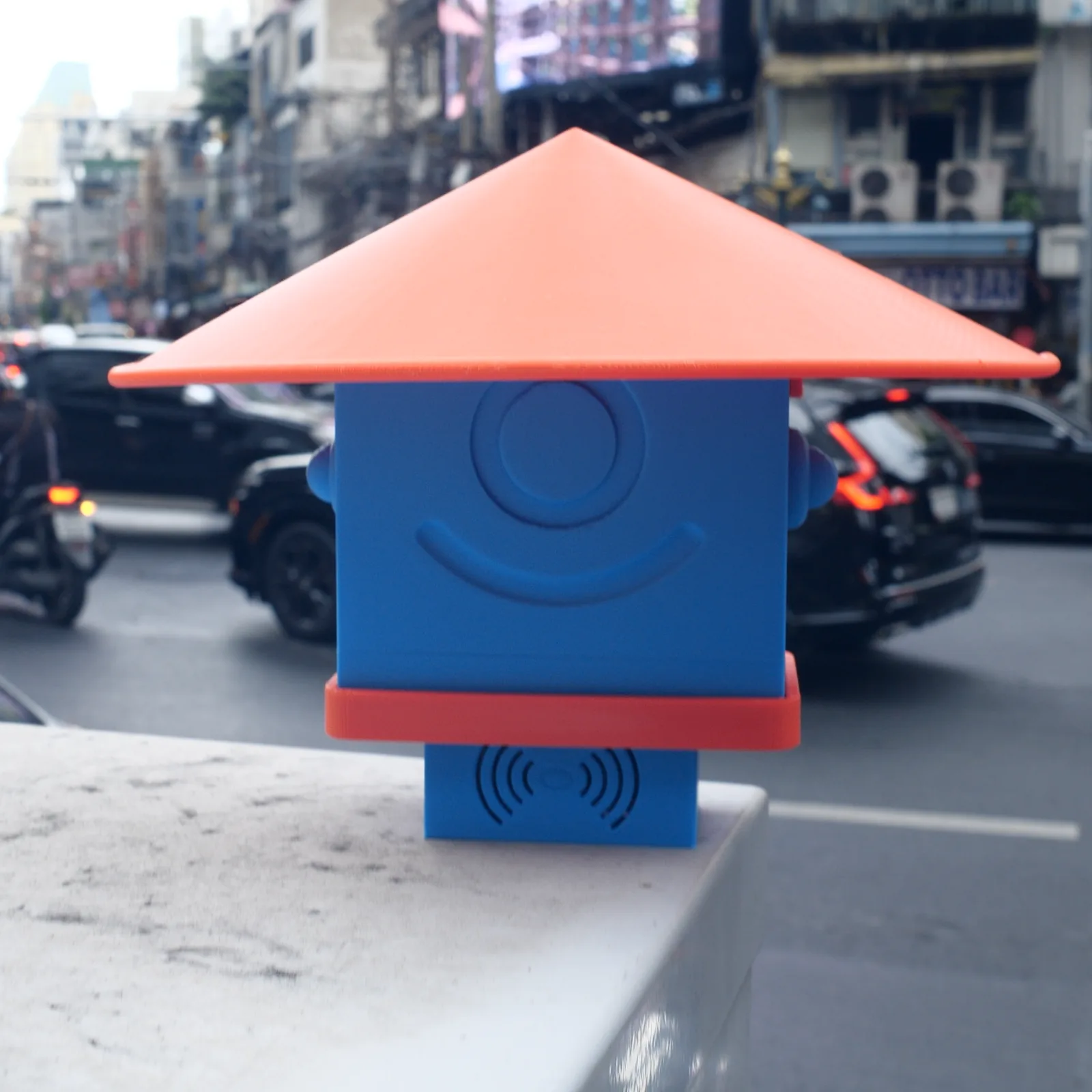 A blue Altruist on a kerbside wall with Bangkok traffic behind it